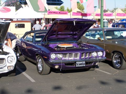 1990 Ford Bronco - A purple Plymouth Barracuda is displayed with its hood open at an outdoor event, alongside other vehicles.