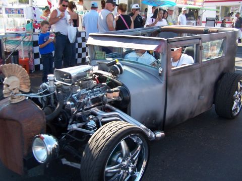 1990 Ford Bronco - A custom rat rod with a mohawk skull on the hood and a powerful engine is on display at an outdoor event.