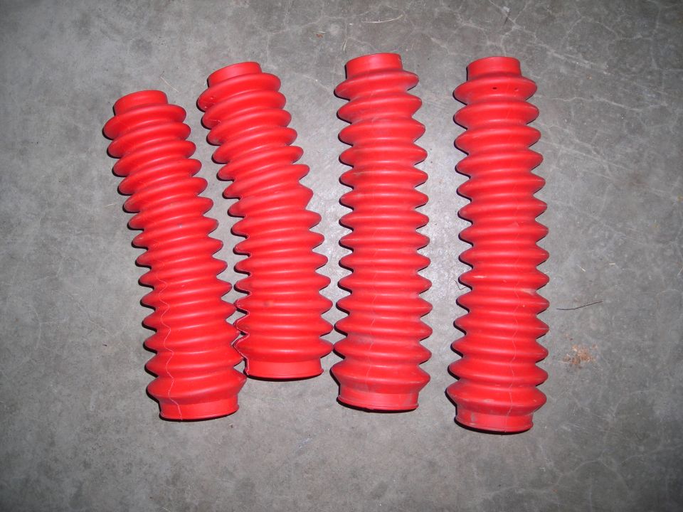 Four red accordion-style dust boots laid out on a gray concrete surface