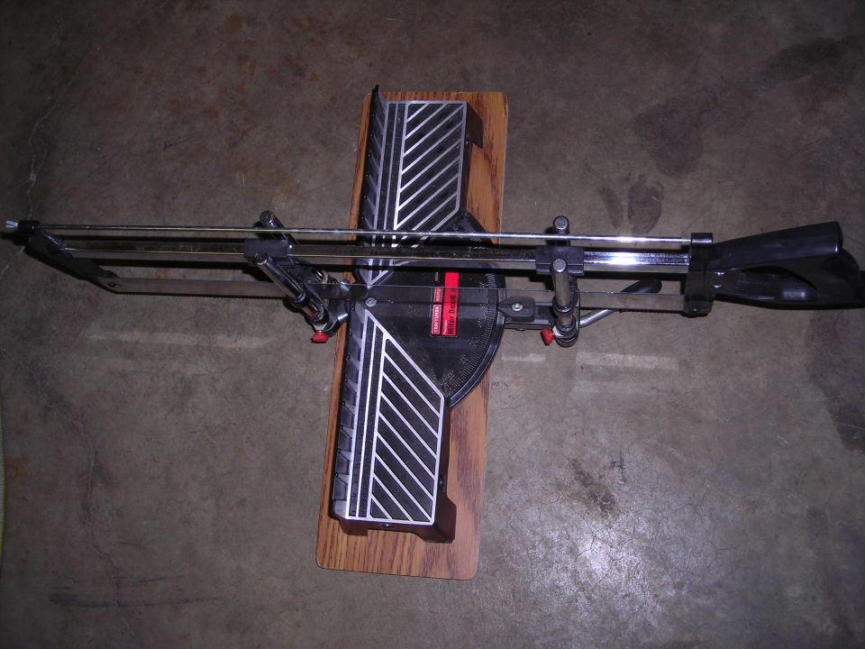 Miter saw on a wooden base, viewed from above. Black and silver metal construction with red accents