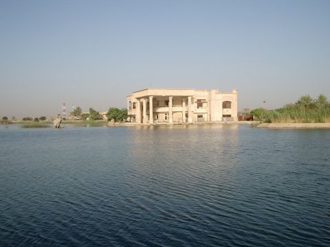 1996 Ford Bronco - A large, classical-style building stands on the water's edge, surrounded by calm blue water and vegetation.