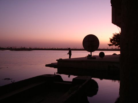 1996 Ford Bronco - A lone figure fishes from a dock as the sun sets, casting a purple hue over the water and silhouetting a boat and a large dish.