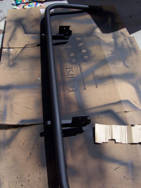 1991 Ford Bronco - A black metal tube bumper is laid out on cardboard, possibly for painting or fabrication.