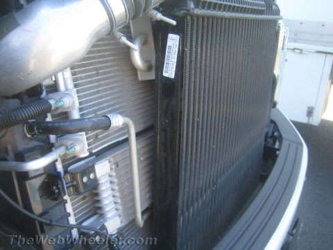 1968 Ford Mustang - Close-up of a vehicle's radiator and condenser assembly, showing various hoses and a label.