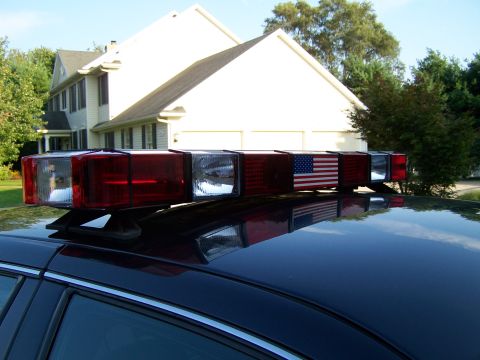 2003 Ford Crown Victoria - Light bar with American flag decal mounted on the roof of a dark car, with a house in the background.