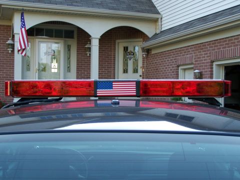 2003 Ford Crown Victoria - A light bar with an American flag is mounted on the roof of a dark vehicle.