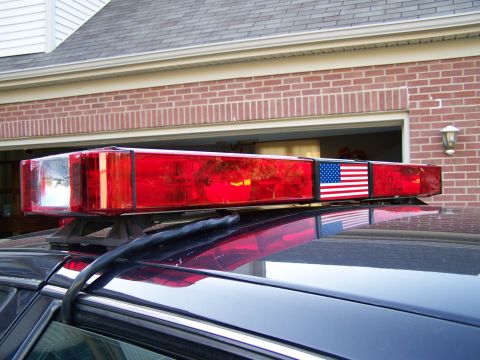 2003 Ford Crown Victoria - A red emergency light bar with an American flag decal is mounted on the roof of a dark-colored vehicle.