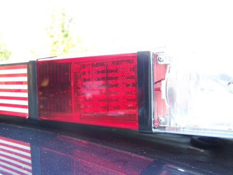 2003 Ford Crown Victoria - Close-up of a rectangular red tail light lens with a clear backup section mounted at the rear of a vehicle outdoors.