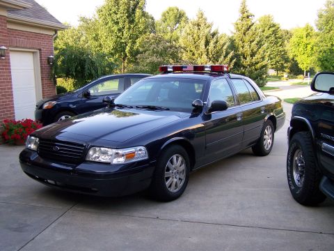 2003 Ford Crown Victoria - A dark blue 2003 Ford Crown Victoria police car is parked in a driveway, equipped with a light bar on its roof.