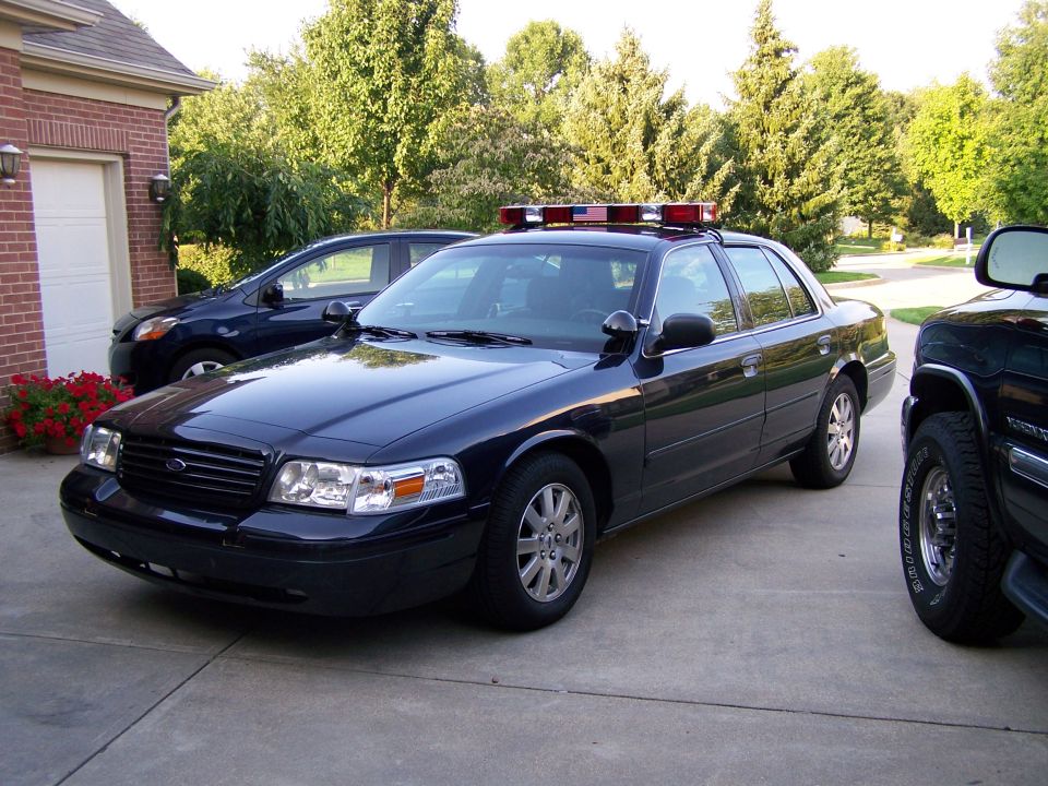 Dark blue 2003 Ford Crown Victoria police car with light bar parked in driveway