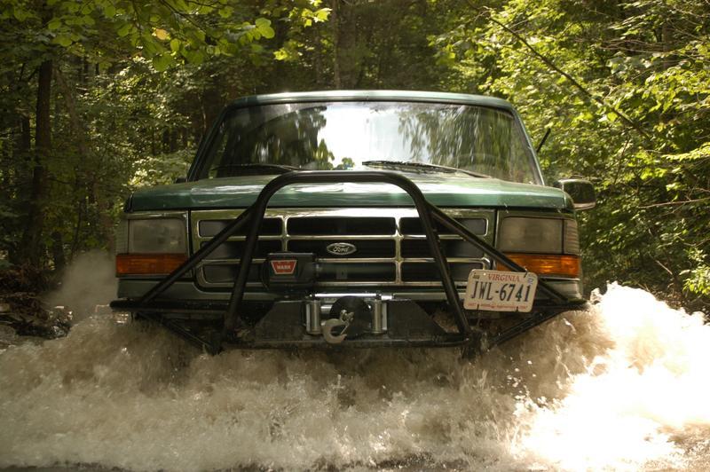 Green Ford Bronco with WARN winch bumper pushing through water crossing, head-on view