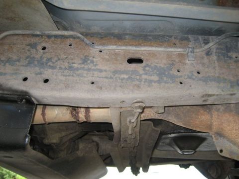 1995 Ford Bronco - Close-up view of the undercarriage of a vehicle, showing the frame and exhaust system with signs of rust.
