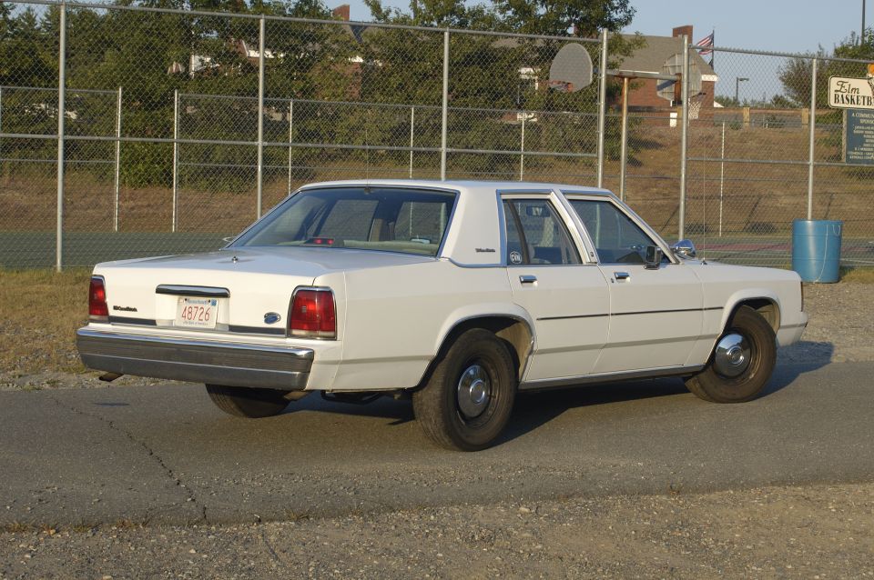 White sedan parked on asphalt, rear quarter view. License plate reads 48726
