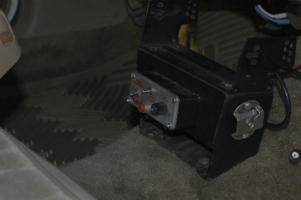Aftermarket control box with red button, knob, and switches mounted on the floor of a vehicle