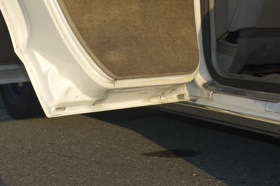 White car door sill with brown carpet trim and visible damage
