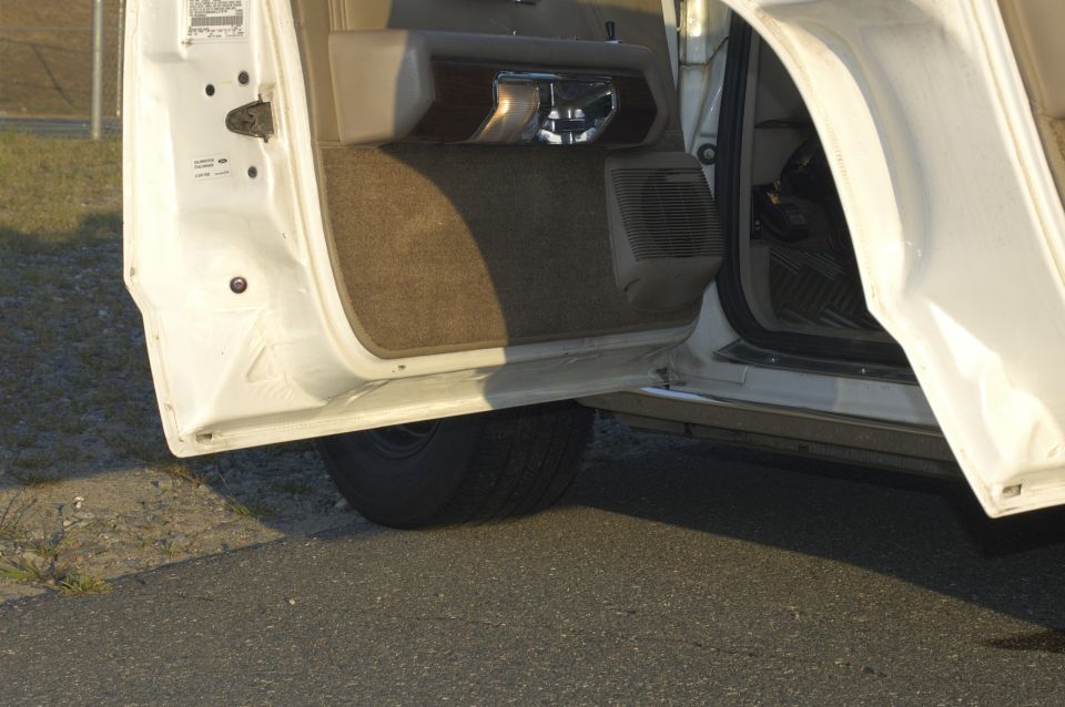 Open driver's side door of a white car, showing the interior door panel, speaker, and part of the seat