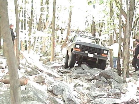 1978 Ford Bronco - An SUV is shown off-roading through a dense, rocky forest environment.