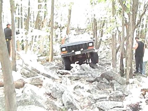 1978 Ford Bronco - A 1978 Ford Bronco is shown off-roading on a challenging, rocky path through a wooded area.