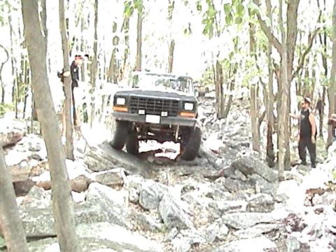 1978 Ford Bronco - A 1978 Ford Bronco navigates a challenging rocky trail through a wooded area.