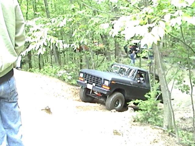 Black 1978 Ford Bronco driving off-road through trees