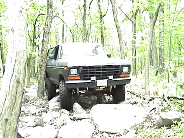 1978 Ford Bronco driving over rocks in a wooded area