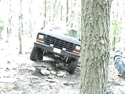 1978 Ford Bronco - A dark Ford Bronco navigates a rocky, wooded terrain.