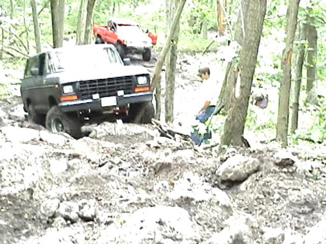 Black 1978 Ford Bronco off-roading on a muddy hill, front 3/4 view