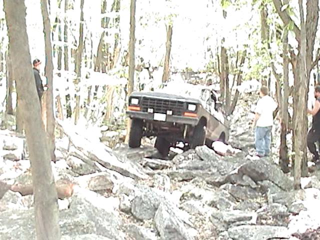 SUV navigating a rocky, wooded trail with people watching