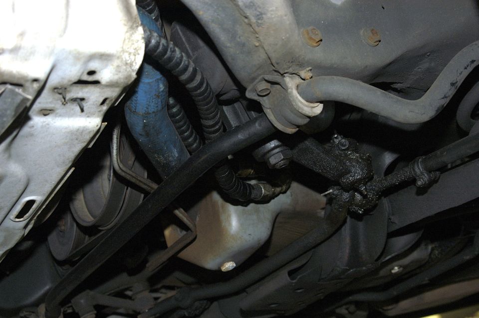 Underside view of a vehicle's steering and suspension components, showing a sway bar, tie rods, and some greasy parts