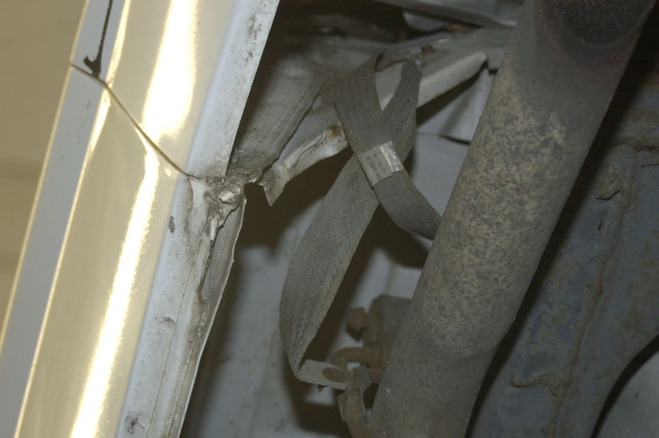 White vehicle undercarriage showing damaged metal and straps near exhaust pipe