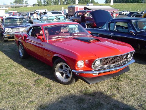 1964 Ford Fairlane - A red 1969 Ford Mustang is parked at an outdoor car show with other vehicles visible.