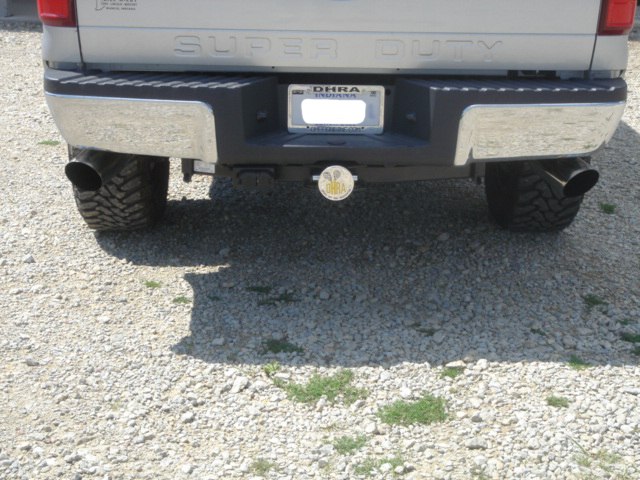 Rear of silver Ford Super Duty pickup with dual black exhaust tips and Indiana plate on gravel