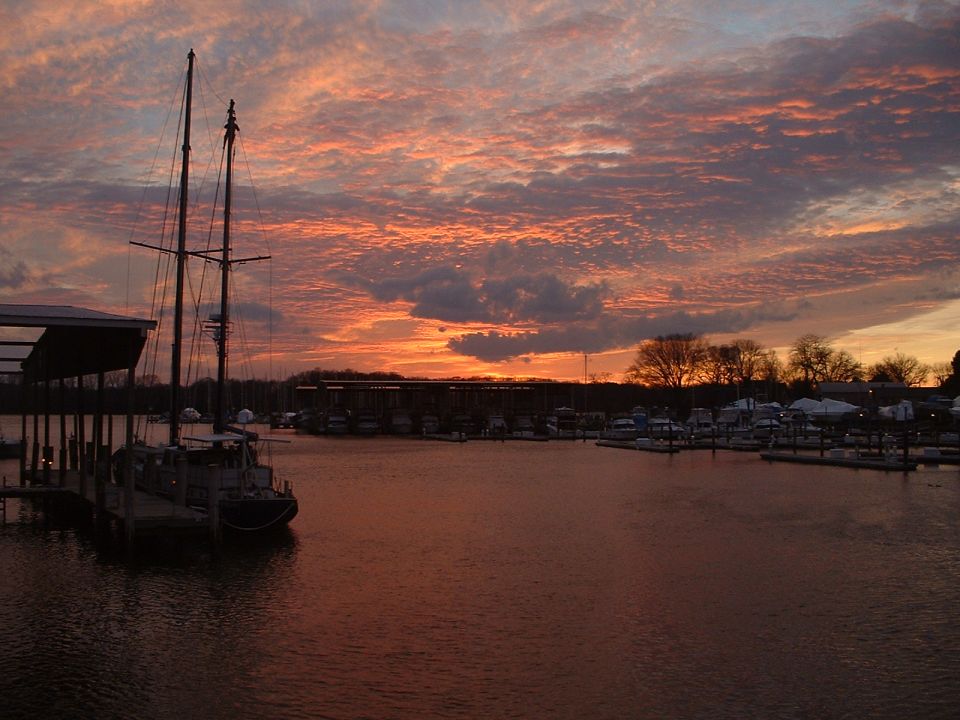 Sailboat docked in marina with colorful sunset sky and other boats in background