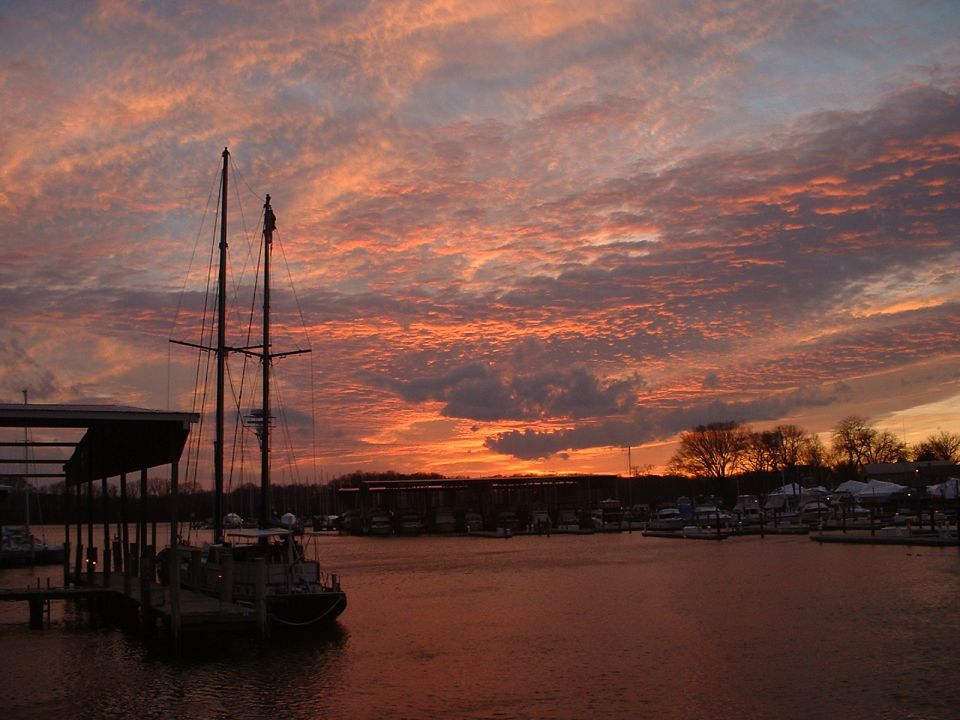 Sailboat docked in marina with colorful sunset sky and other boats in background