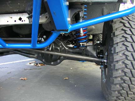 1984 Ford Bronco - Close-up view of the undercarriage and suspension system of an off-road vehicle, a prominent blue roll cage and a large tire.