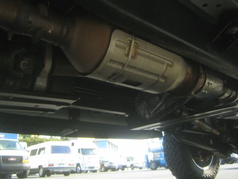 1968 Ford Mustang - Undercarriage of a vehicle, showing exhaust system and drivetrain components. Other vehicles are parked in the background.