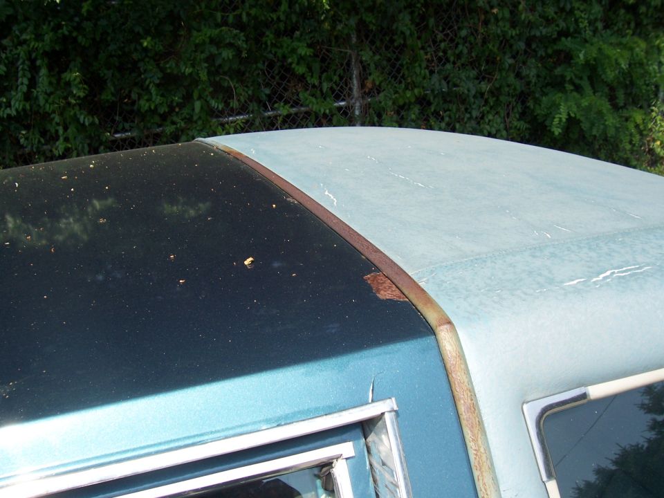 Close-up of a car's roofline showing a dark upper section and a lighter blue lower section with rust on the trim