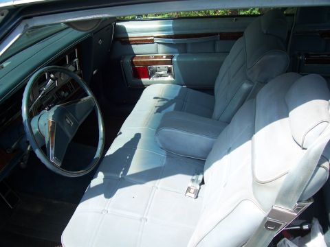 1999 Ford Crown Victoria - The interior of a vintage car features light blue bench seats, wood trim accents, and a prominent blue steering wheel.