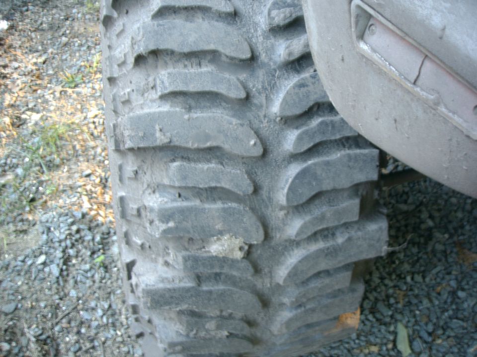 Close-up of aggressive mud-terrain tire tread and lugs on a truck parked on gravel