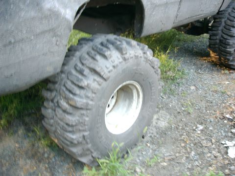 1991 Chevrolet Suburban - A vehicle with large, aggressive tires is parked on a gravelly surface with some grass.