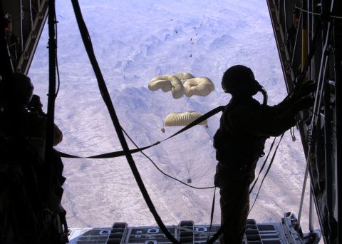1988 Ford Bronco - Paratroopers exit an aircraft over a barren, mountainous terrain.