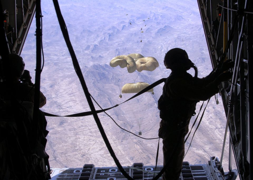 View from inside an aircraft as paratroopers jump into a mountainous landscape