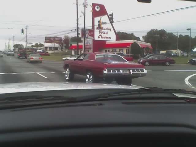 Dark red 1970s coupe turning at an intersection past a Kentucky Fried Chicken