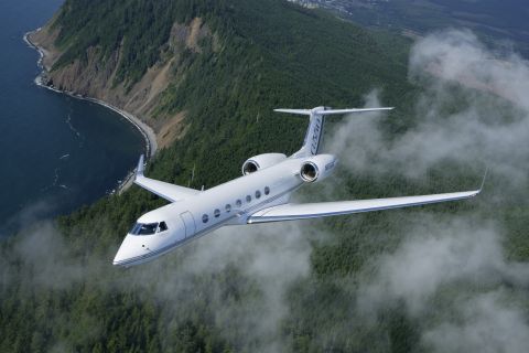 1990 Ford Mustang - A white private jet cruises through the sky above a misty, tree-covered coastline.