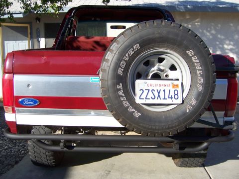 1991 Ford Bronco - Rear view of a red Ford Bronco a spare tire mounted on the back and a custom metal bumper.
