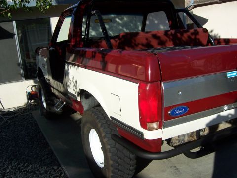 1991 Ford Bronco - The rear section of a two-tone red and white Ford Bronco is visible, a Ford emblem and a chrome trim piece.