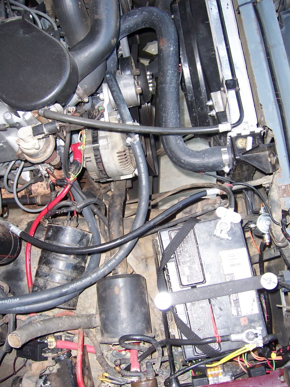 Engine bay view showing battery, radiator hoses, alternator, and fan