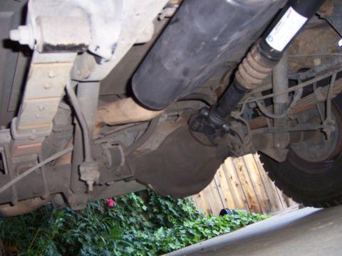 1991 Ford Bronco - The undercarriage of a vehicle shows the rear axle assembly and driveshaft, with a white label attached to the driveshaft.