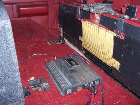 1991 Ford Bronco - An aftermarket amplifier is installed in the rear of a vehicle with red carpeting and visible wiring.