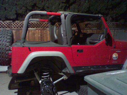 1994 Ford Bronco - A red Jeep Wrangler is parked outdoors with a spare tire mounted on the rear and a soft top in place.
